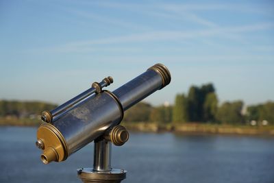 Close-up of coin-operated binoculars by lake against sky