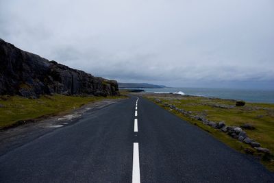 Empty road by sea against sky