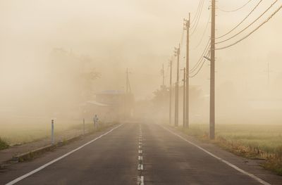 Empty road by electricity pylons during foggy weather