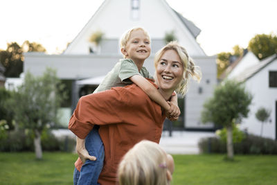 Happy mother giving piggyback ride to daughter in back yard