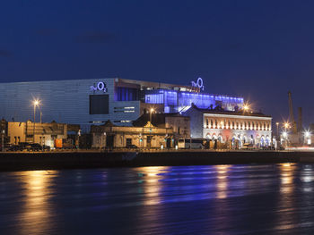 Illuminated buildings by river against sky at night