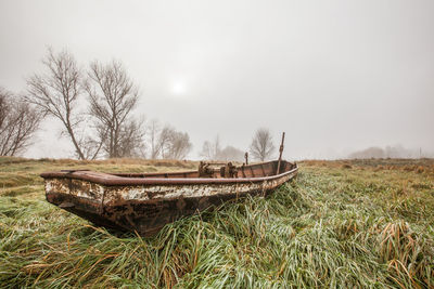 Abandoned boat moored on field against sky