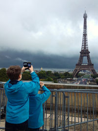 Siblings photographing eiffel tower against sky in city