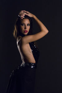 Young woman wearing backless dress while posing against black background