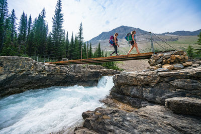 Backpackers crossing glacial river on foot bridge along whaleback