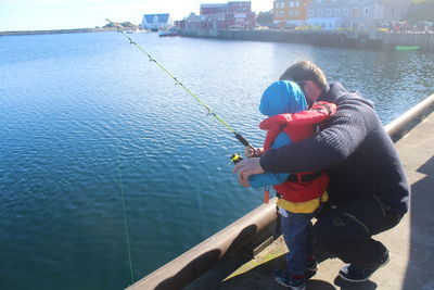 Full length of father and son fishing at harbor during sunny day