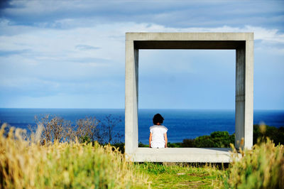 Girl sitting in concrete square and looking at sea