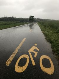 Arrow sign on road against sky during rainy season