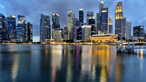 Sea by illuminated buildings against sky