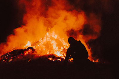 Silhouette man sitting by bonfire at night