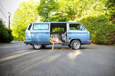 Two girls sitting doorway of vintage van on street looking at camera