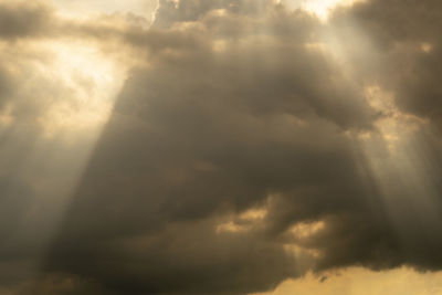 Low angle view of sunlight streaming through clouds