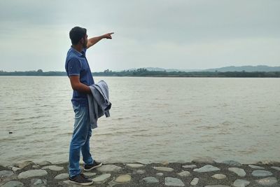 Full length of man gesturing white standing on pier over river against sky