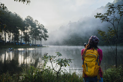 Rear view of woman standing by lake against sky