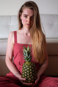 Portrait of beautiful young woman holding pineapple at home