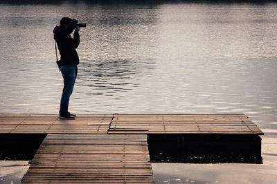 Full length of man photographing with camera while standing on pier over lake