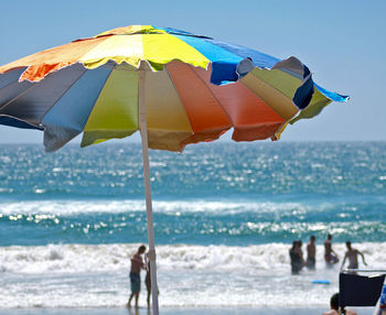 Colorful parasol at beach with people in sea during sunny day