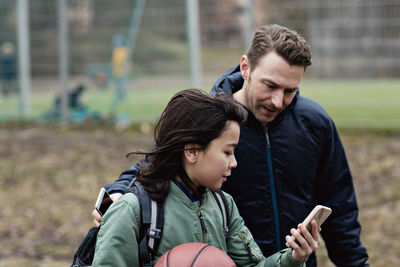 Son showing his smart phone to father while standing by sports court