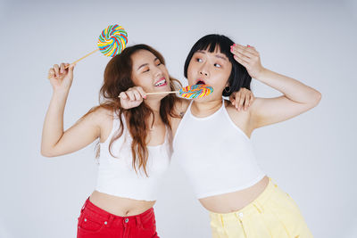 Lesbian couple holding lollipop against white background