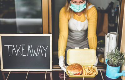 Young woman preparing takeaway food inside restaurant during coronavirus period - focus on hamburger