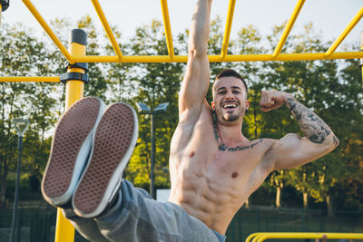 Portrait of smiling shirtless man jumping against sky