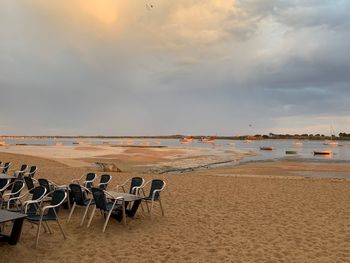 Empty chairs on beach against sky during sunset