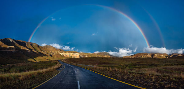 Empty road against rainbow in blue sky at golden gate highlands national park