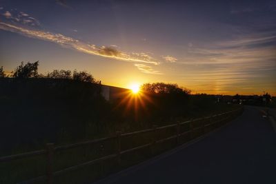 Road amidst silhouette trees against sky during sunset