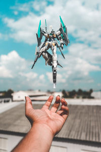 Cropped image of person holding airplane against sky