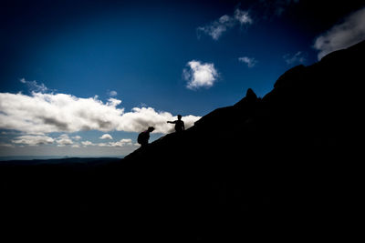 Silhouette of two people climbing mountain