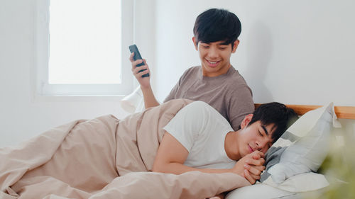 Smiling man looking at partner sleeping on bed at home