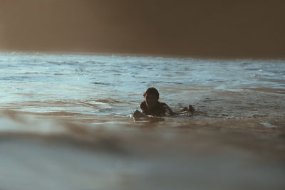 Surfer lying on surfboard at sunset