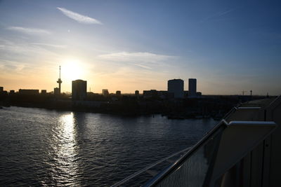 Buildings by river against sky during sunset