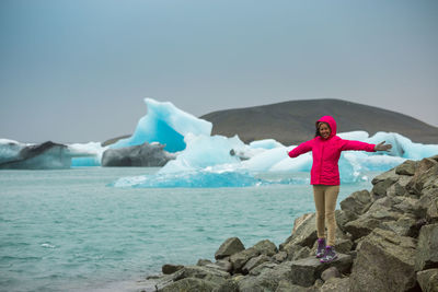 Woman standing on rock by sea against sky