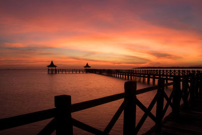 Silhouette pier over sea against orange sky