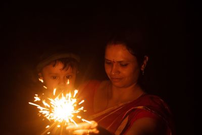 Midsection of woman holding sparkler at night