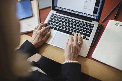 Cropped image of senior woman's hands using laptop at table in law library