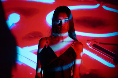 Serious brunette in black nightwear in studio with glowing red and white light illumination from projector looking at camera with self confidence