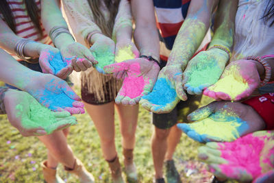 Low section of friends showing hands covered with multi color face paints at carnival