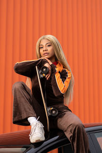 Young african american woman with long blonde hair and sportswear on an orange background