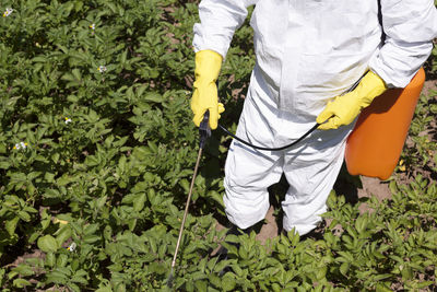 Midsection of farmer spraying pesticide on plants