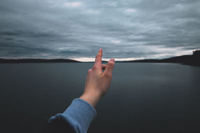 Cropped image of hand gesturing against lake during sunset