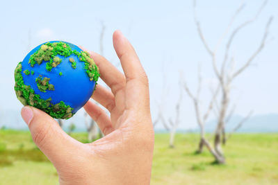 Cropped hand of person holding earth ball against sky