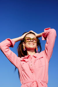 Young woman with arms raised standing against clear blue sky