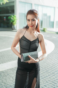 Portrait of smiling woman in black dress standing outdoors