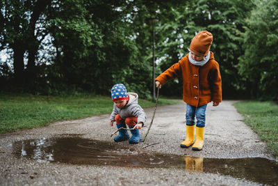 Front view of young male kids playing with sticks in a puddle in park