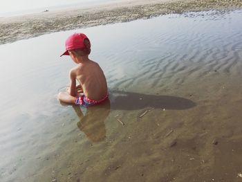 Rear view of shirtless boy sitting in water at beach