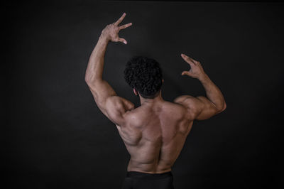 Rear view of shirtless man standing against black background