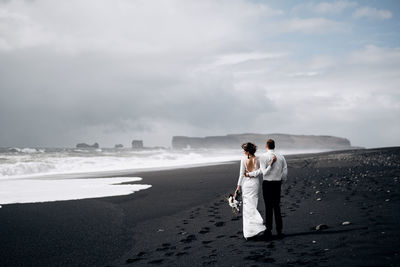 Couple standing on beach against sky