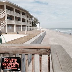 No trespassing sign on beach by sea against sky